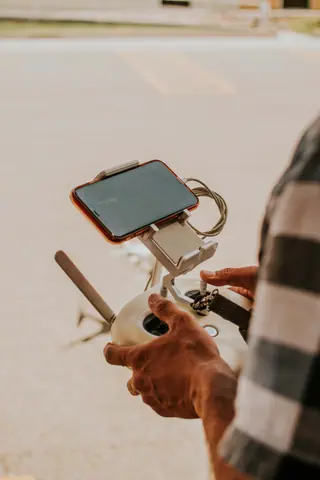 Close-up of hands holding a drone controller with smartphone outdoors.