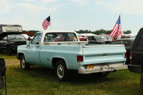 Classic Chevrolet pickup truck displayed at an outdoor car gathering with American flags.