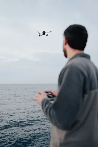 A man controls a flying drone over the ocean, showcasing modern technology and hobbyist interests.