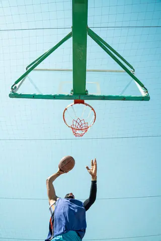 Low angle shot of a basketball player making a shot against a clear blue sky.