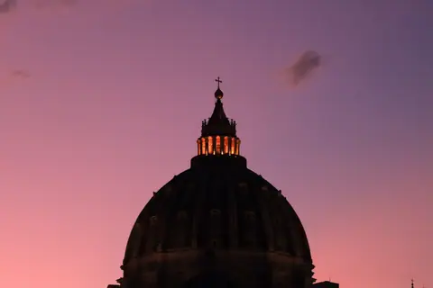 Sunset view of St. Peter's Basilica silhouette with a vibrant pink sky in Vatican City.