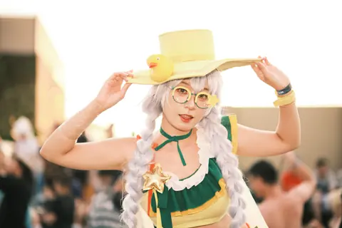 Vibrant cosplay character with yellow hat and unique accessories at an outdoor event.