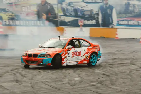 Vibrant drift car in a dynamic maneuver at an outdoor racing event, emitting tire smoke.