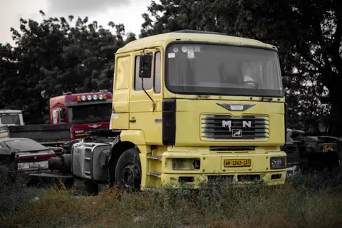 A yellow truck cab parked in an outdoor lot surrounded by other vehicles and trees.