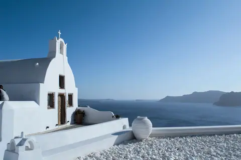 Whitewashed church in Santorini with panoramic Aegean Sea view under a clear blue sky.