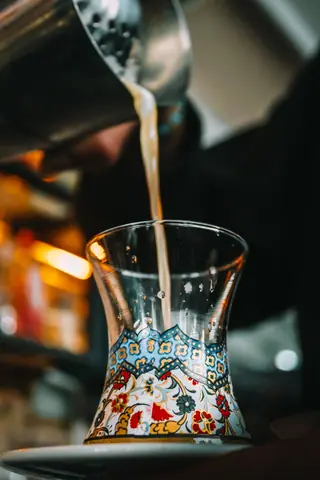 Artistic shot of tea being poured into a beautifully decorated glass. Warm tones.