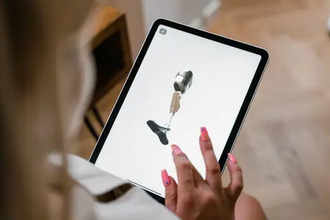 A woman interacts with a digital illustration of a prosthetic leg on a tablet screen.