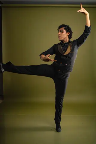 A male flamenco dancer in a dynamic pose wearing a black suit against a studio backdrop.