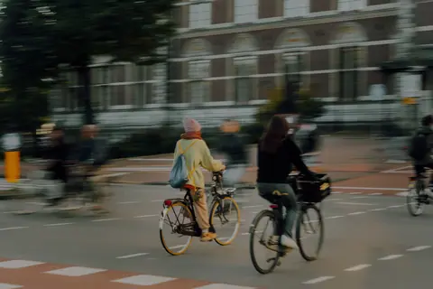 Blurred cyclists riding through Amsterdam street at dusk, showcasing urban commuting culture in the Netherlands.
