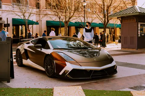Sleek Lamborghini Gallardo parked outdoors with people in background, urban setting.