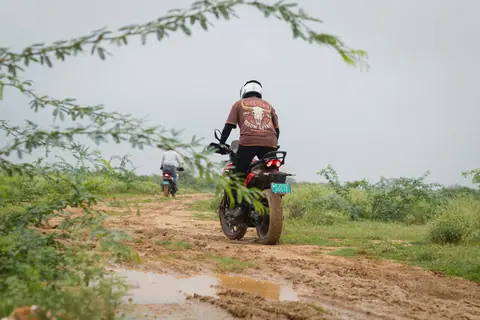 Two motorcyclists navigating muddy trails in Jaipur, India.