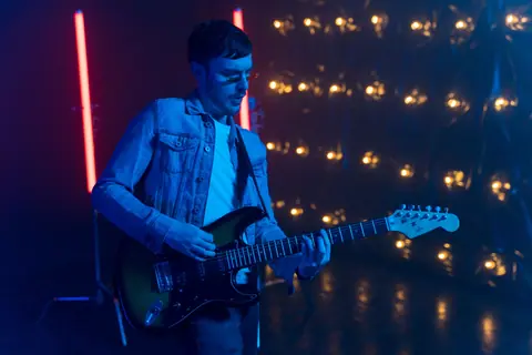 Musician playing electric guitar under blue neon lights, creating a vibrant concert atmosphere.