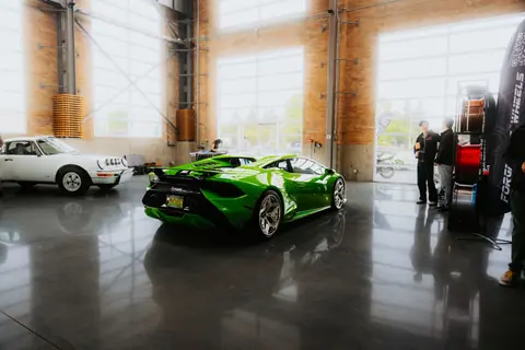Green Lamborghini and classic car displayed in a sleek, modern showroom interior with people observing.