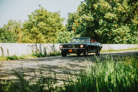 A vintage black convertible driving on a sunny road through lush green scenery, perfect for travel enthusiasts.