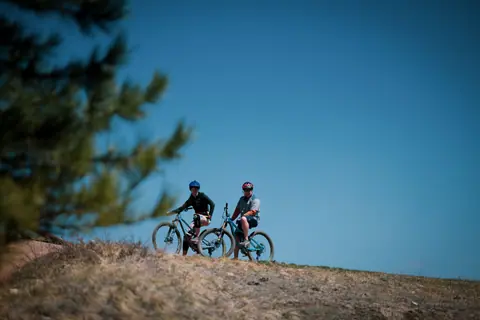 Two cyclists enjoying a relaxed ride atop a scenic hill under a clear blue sky.