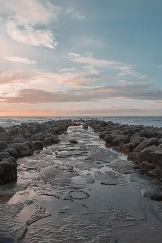 Peaceful rocky pathway leading into the ocean at sunset in Middelkerke, Belgium.