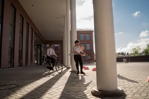 Two men enjoy skateboarding and biking in a modern urban environment on a sunny day.