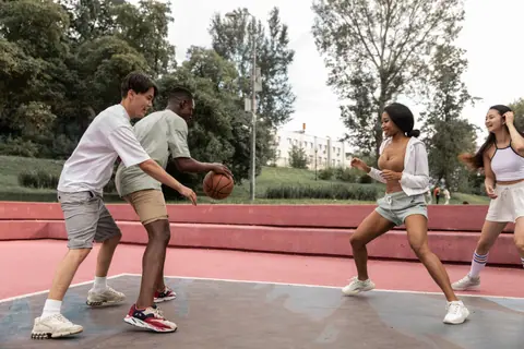 Cheerful young multiracial sportspeople in activewear playing basketball on sports ground in lush city park