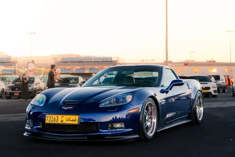A sleek blue sports car parked outdoors during sunset at a gathering, showcasing urban details.