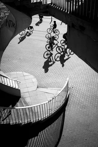 Artistic black and white photo of cyclists and their shadows on a city spiral path.