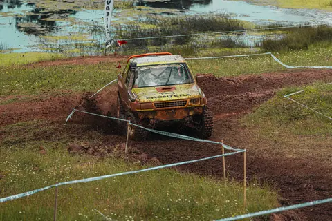 An off-road vehicle racing through a muddy, challenging course in outdoor environment.