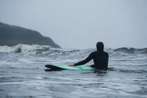 Surfer in wetsuit paddling on the ocean with overcast skies, ready to ride waves.