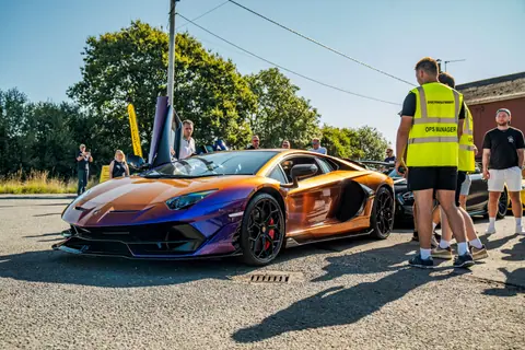 Vibrant orange luxury sports car showcased in a UK parking lot during a sunny day event.