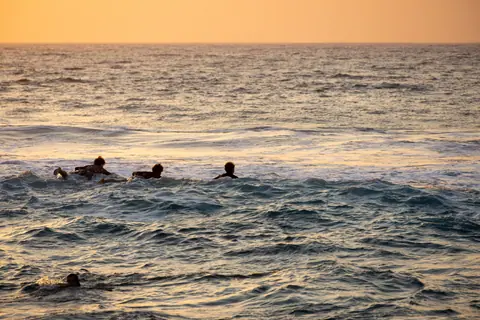 Silhouetted surfers enjoying the ocean waves during a stunning sunset.