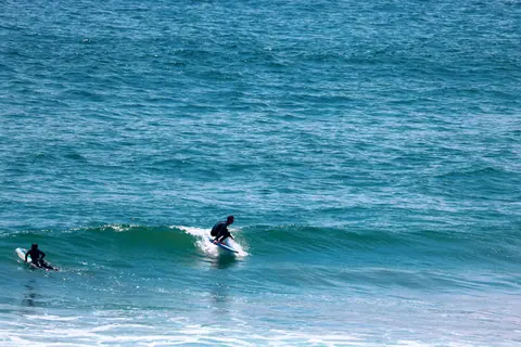 Two surfers expertly navigating waves on a sunny day at sea.
