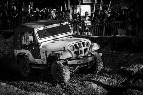 Exciting offroad Jeep driving through a muddy terrain during a racing event with spectators watching.