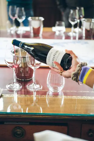 Hand pouring red wine into glass on table at tasting event.