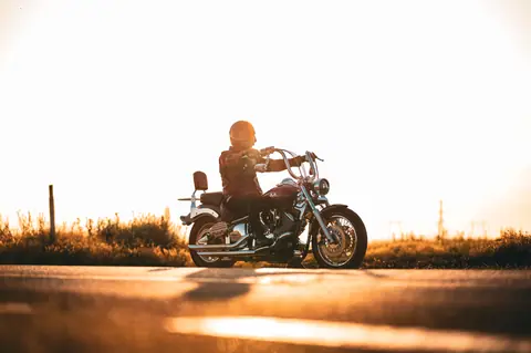 A motorcyclist in a helmet rides along a sunlit road at sunset, symbolizing freedom.