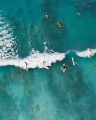 Aerial shot capturing surfers enjoying the ocean waves, showcasing water sports adventure.
