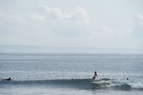 Person surfing on a gentle wave under a clear sky, embracing the thrill of ocean adventure.
