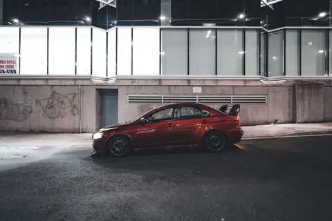 A red sports sedan parked on an urban street at night in front of modern architecture.