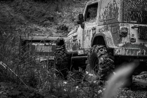 A muddy jeep tackling off-road terrain in a rural setting, showcasing adventure and ruggedness.