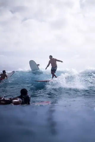 Group of unrecognizable people enjoying riding surfboard in wavy sea water in cloudy day