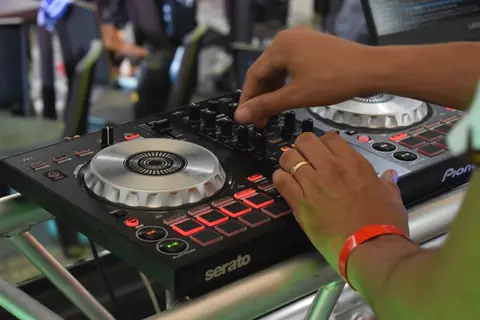 Hands adjusting DJ sound mixer with modern electronics in a lively concert setting.