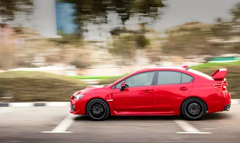 Red sports car in motion on a city road with a blurred background, showcasing speed.