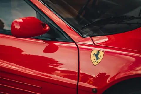 Detailed shot of a red luxury sports car with prominent emblem, showcasing sleek design.