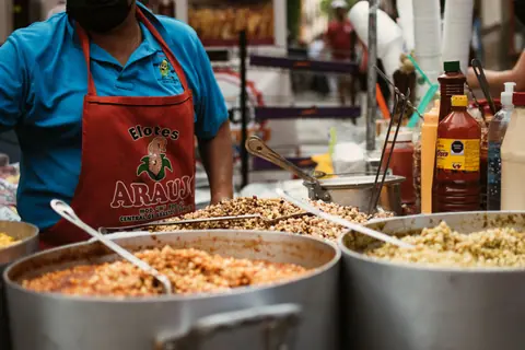A street vendor in Guanajuato, Mexico serving various Mexican corn dishes from large pots outdoors.
