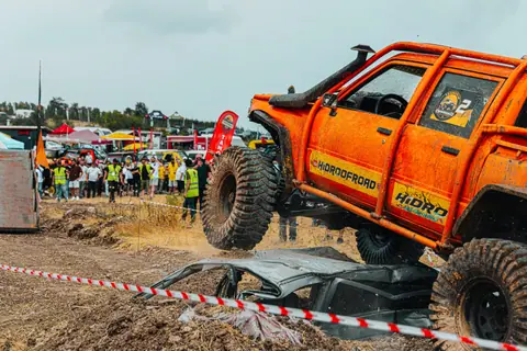 An orange off-road truck crushing cars in an exciting outdoor competition with spectators watching.