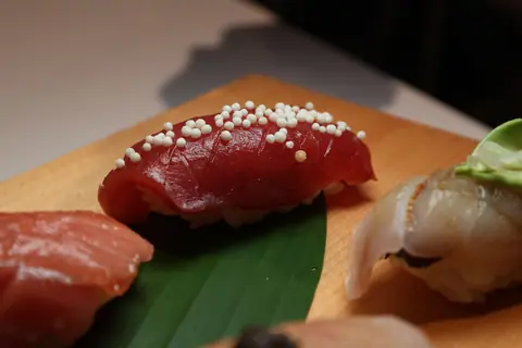 Delicious sushi nigiri with fresh tuna and garnishes served on a wooden plate.