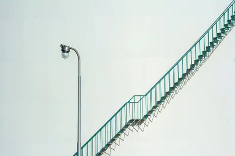 A minimalist view of an industrial staircase and street light against a white backdrop.