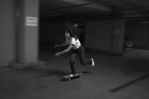 Blurred motion capture of a woman skateboarding indoors in monochrome.
