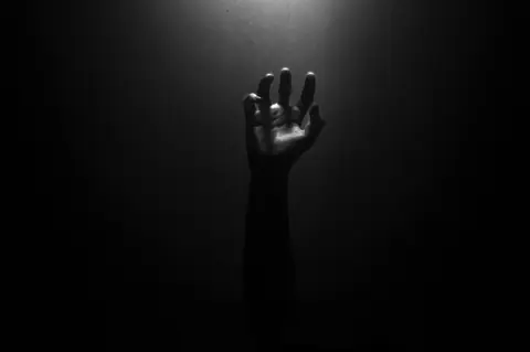A solitary hand reaching upward contrasted against a dark backdrop, creating an eerie effect.