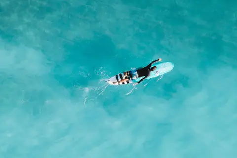 Top view of surfer paddling on bright turquoise water, capturing the essence of a summer adventure.