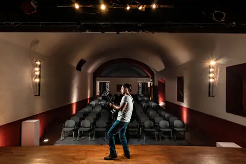 A lone musician playing guitar on stage in a dimly lit, empty concert hall.