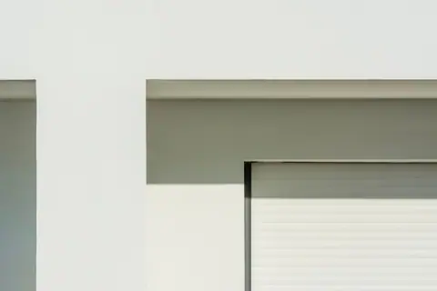 Minimalist white building facade with sunlit shadows creating geometric patterns.