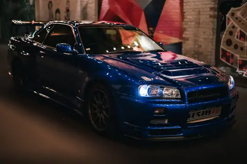 A striking blue sports car parked in a vibrant urban mural street at night.
